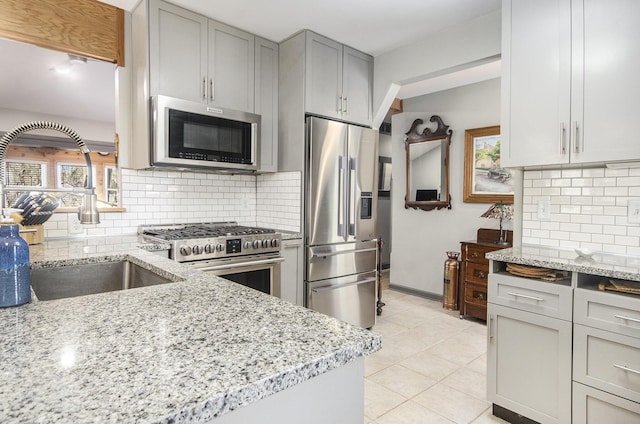 kitchen with light tile patterned floors, light stone counters, a sink, stainless steel appliances, and decorative backsplash