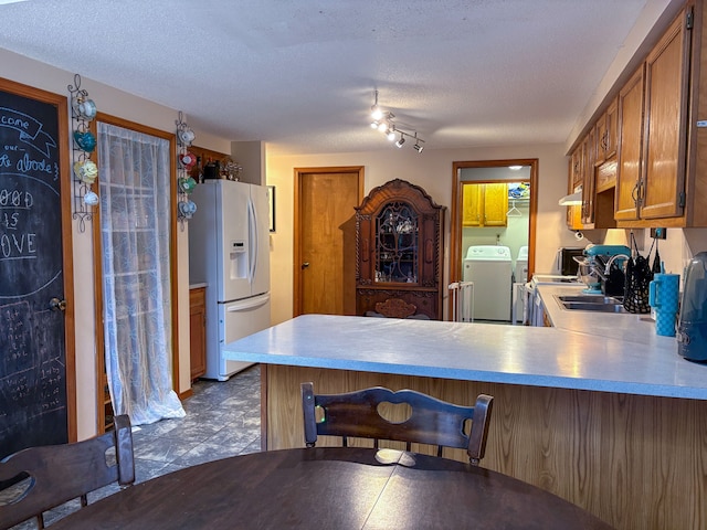 kitchen with white refrigerator with ice dispenser, a peninsula, washer and dryer, light countertops, and a textured ceiling