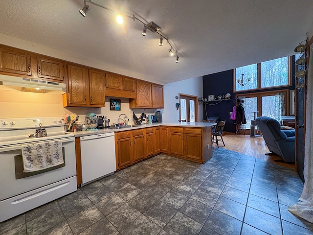 kitchen featuring white appliances, under cabinet range hood, a peninsula, a sink, and brown cabinetry