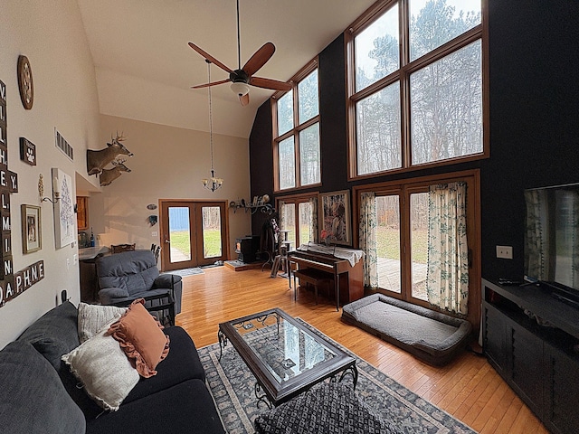 living area featuring high vaulted ceiling, light wood finished floors, ceiling fan, and a chandelier