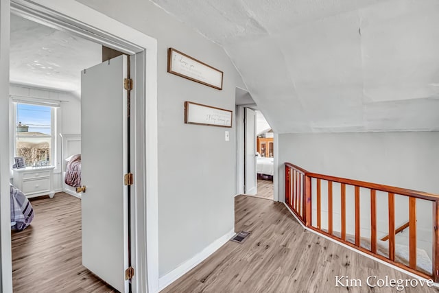 hallway featuring visible vents, vaulted ceiling, wood finished floors, an upstairs landing, and baseboards