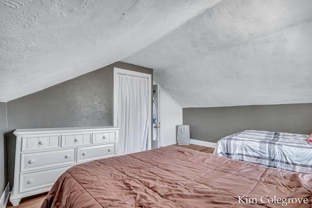 bedroom with a textured ceiling, wood finished floors, and lofted ceiling