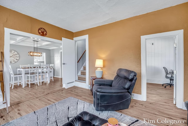 living room featuring coffered ceiling, wood finished floors, baseboards, and stairway
