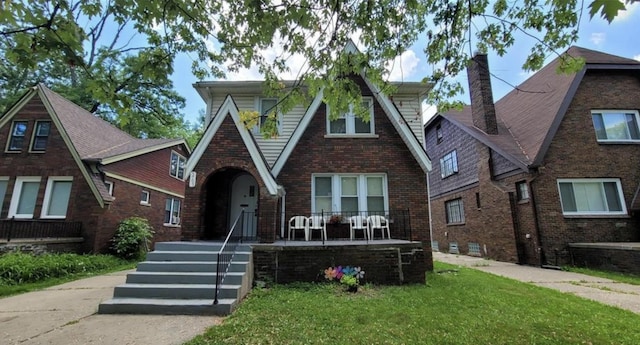 5793 Yorkshire Rd, Detroit, MI 48224 - tudor home featuring a porch, a chimney, a front yard, and brick siding