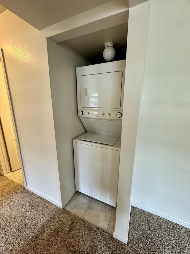 washroom featuring laundry area, light colored carpet, stacked washer / dryer, light tile patterned flooring, and baseboards