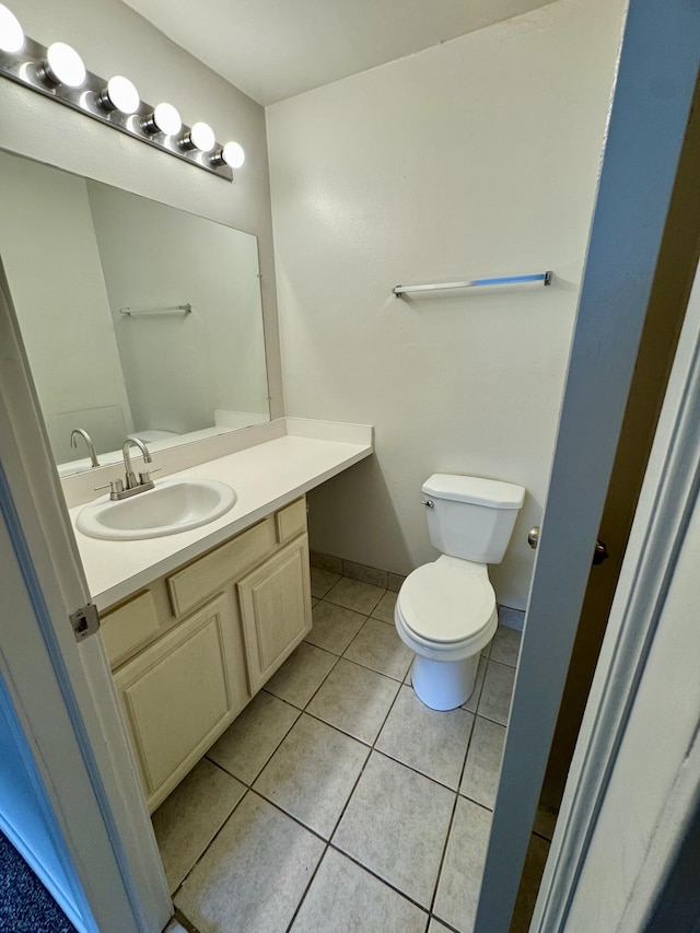 half bathroom featuring tile patterned floors, vanity, baseboards, and toilet