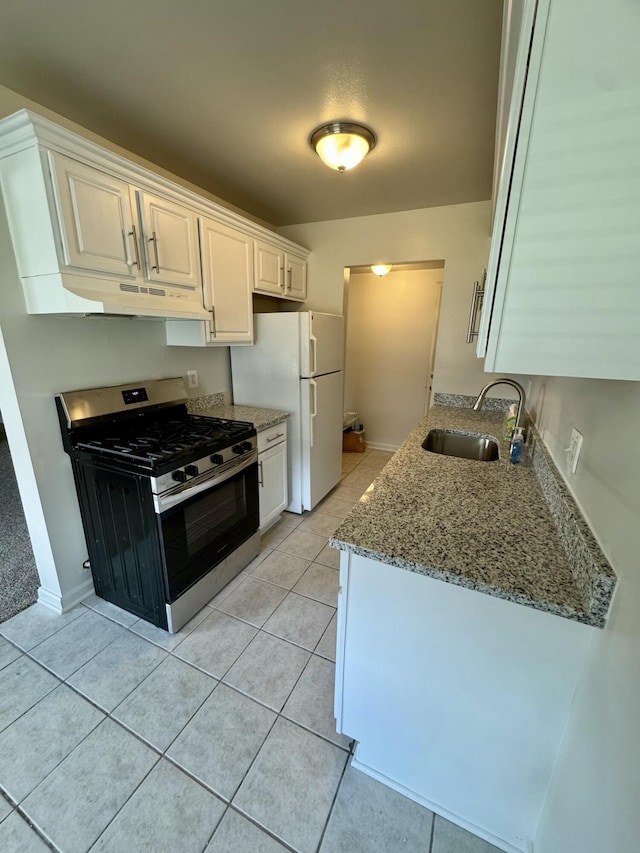 kitchen with gas stove, white cabinetry, freestanding refrigerator, light tile patterned flooring, and a sink