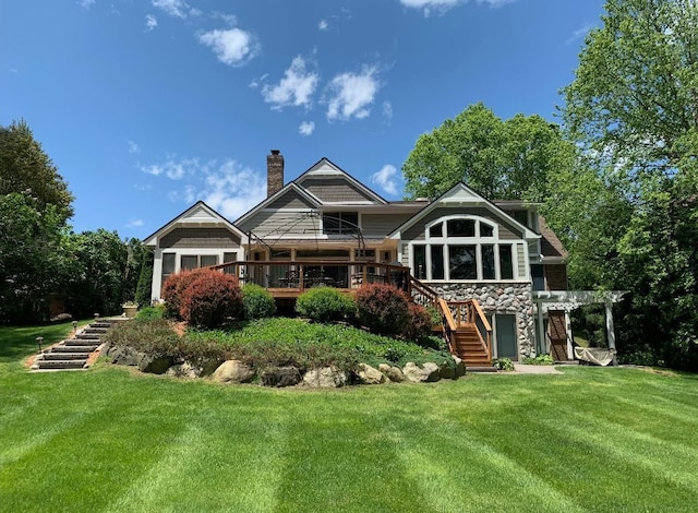 rear view of house with a wooden deck, stone siding, a chimney, stairs, and a yard