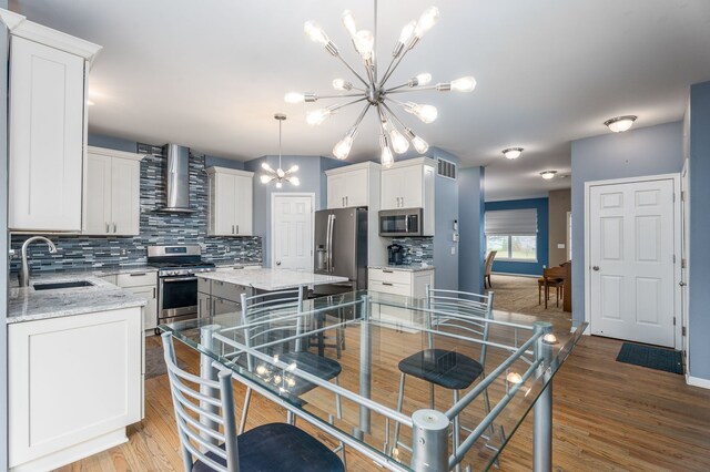 3885 Silver Charm Ln, Howell, MI 48843 - kitchen with stainless steel appliances, a sink, wall chimney range hood, a chandelier, and tasteful backsplash