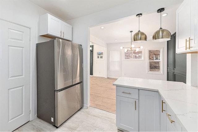 kitchen featuring decorative light fixtures, freestanding refrigerator, a chandelier, a peninsula, and light stone counters
