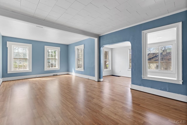 unfurnished living room with arched walkways, wood finished floors, and a wealth of natural light