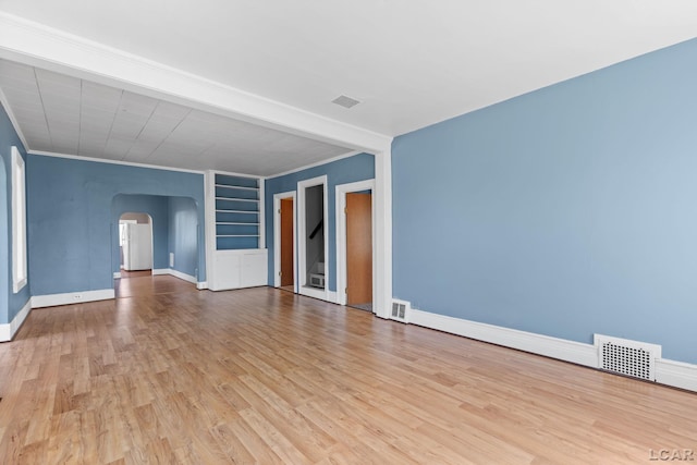 empty room featuring arched walkways, wood finished floors, and visible vents