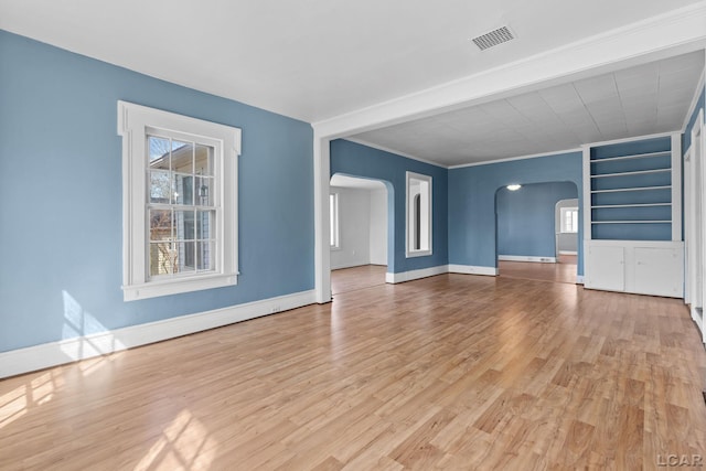 unfurnished living room with visible vents, baseboards, arched walkways, and wood finished floors