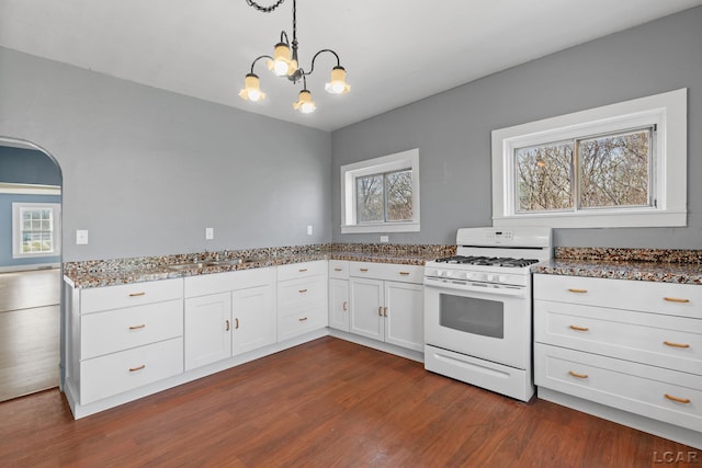 kitchen featuring dark stone counters, an inviting chandelier, white cabinets, gas range gas stove, and dark wood-style floors