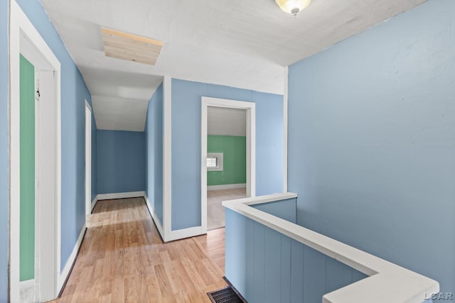 hallway with an upstairs landing, visible vents, baseboards, and light wood-type flooring