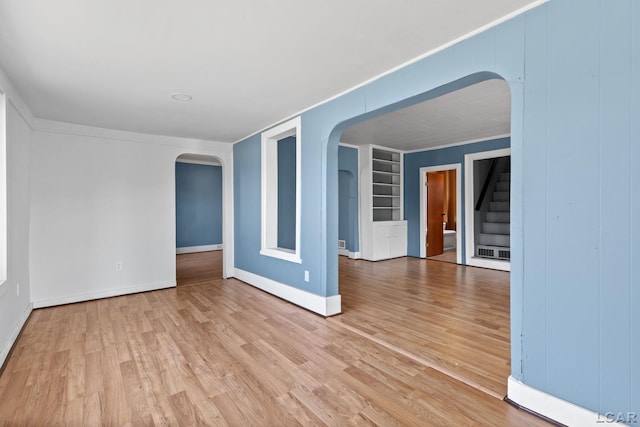 empty room with built in shelves, light wood-type flooring, arched walkways, and stairway