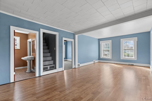 unfurnished living room with wood finished floors, ornamental molding, visible vents, and stairs