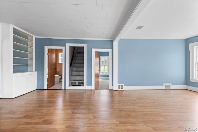 spare room featuring light wood-style flooring, built in features, visible vents, and stairway