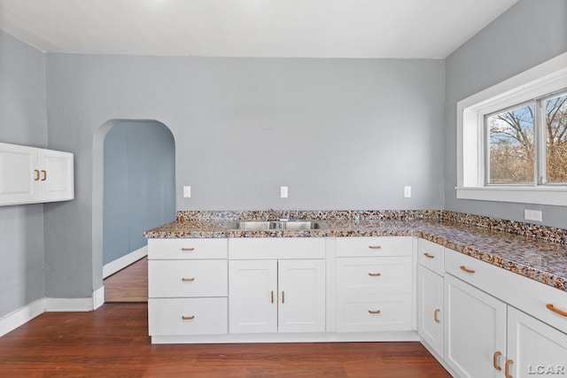 kitchen with a sink, baseboards, white cabinetry, and dark wood finished floors