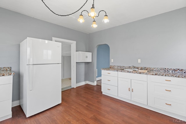 kitchen featuring arched walkways, a notable chandelier, a sink, freestanding refrigerator, and white cabinetry