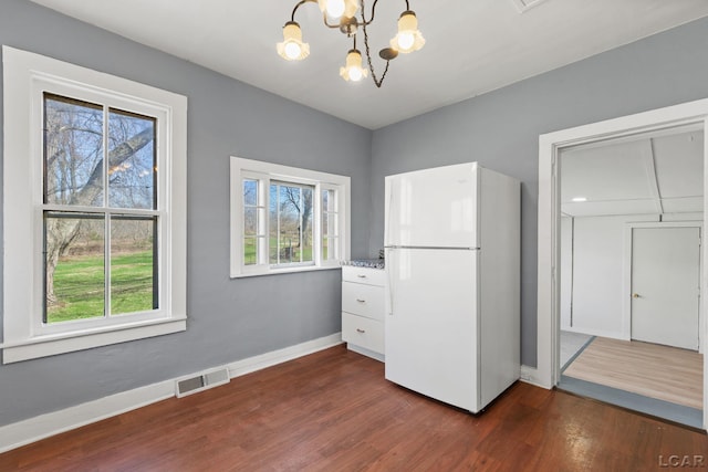 interior space featuring an inviting chandelier, freestanding refrigerator, visible vents, dark wood-style flooring, and baseboards