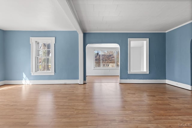 unfurnished living room with arched walkways, baseboards, crown molding, and wood finished floors