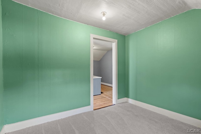 carpeted empty room featuring baseboards and lofted ceiling