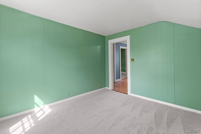 carpeted empty room featuring baseboards and vaulted ceiling