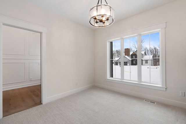 carpeted empty room featuring a chandelier and baseboards