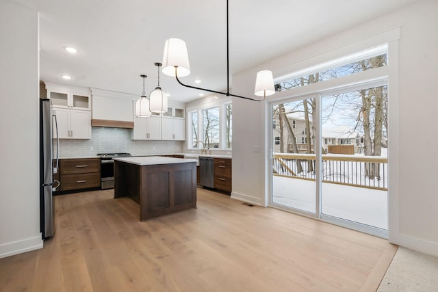 kitchen featuring appliances with stainless steel finishes, a kitchen island, white cabinets, light countertops, and light wood-style floors