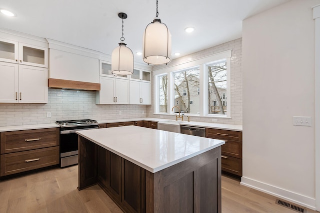 kitchen with appliances with stainless steel finishes, a sink, light countertops, tasteful backsplash, and light wood-type flooring
