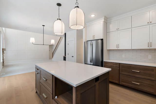 kitchen featuring freestanding refrigerator, light wood finished floors, light countertops, white cabinets, and tasteful backsplash