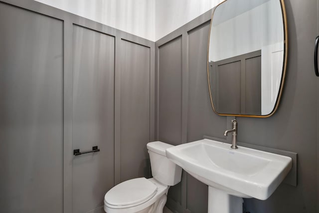 bathroom featuring toilet, a sink, and a decorative wall