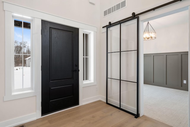 entrance foyer featuring light wood-type flooring, a barn door, wainscoting, and a decorative wall