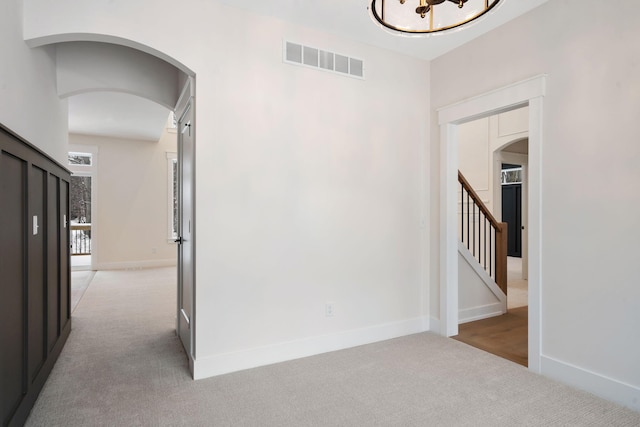 corridor featuring carpet flooring, arched walkways, stairway, and baseboards
