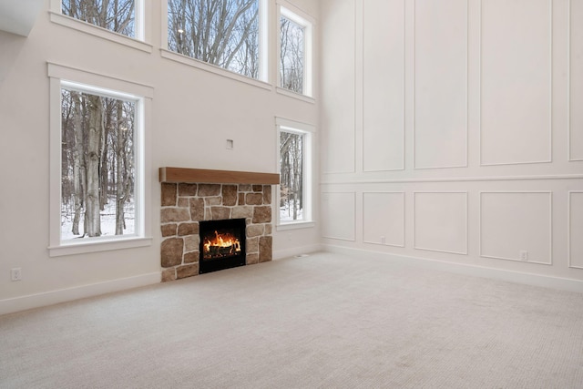 unfurnished living room featuring carpet floors, a fireplace, a high ceiling, and baseboards