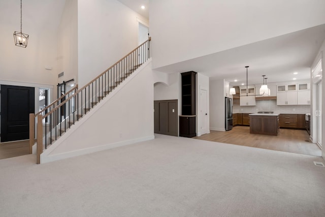 unfurnished living room featuring light carpet, recessed lighting, a towering ceiling, a chandelier, and baseboards