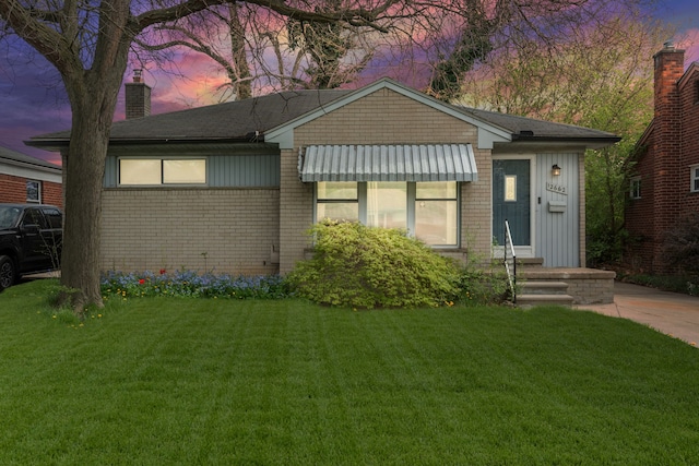 view of front of property with a lawn, a chimney, and brick siding