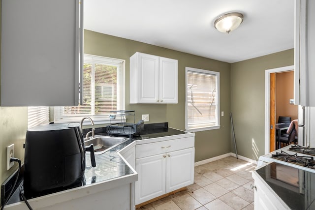 kitchen featuring a sink, baseboards, light tile patterned flooring, and white cabinetry