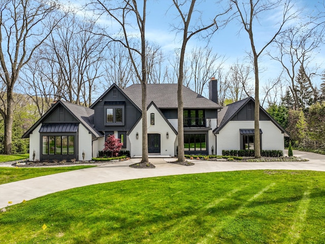 view of front of property featuring a chimney, a balcony, board and batten siding, and a front yard