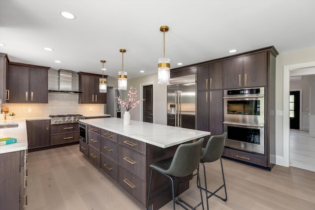 245 Chestnut Cir, Bloomfield Hills, MI 48304 - kitchen featuring wall chimney range hood, appliances with stainless steel finishes, light wood-style flooring, dark brown cabinets, and recessed lighting