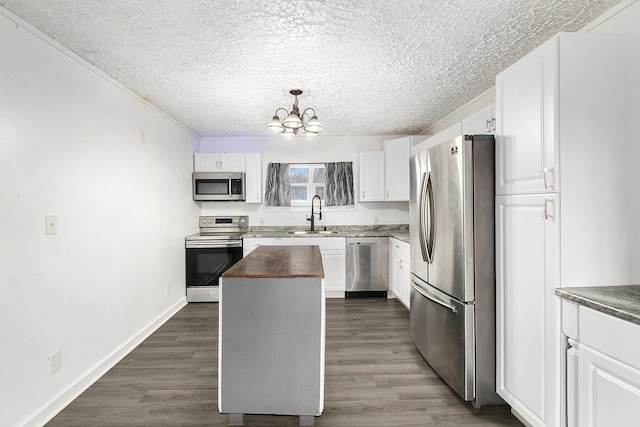 kitchen with a chandelier, butcher block counters, white cabinets, appliances with stainless steel finishes, and a sink