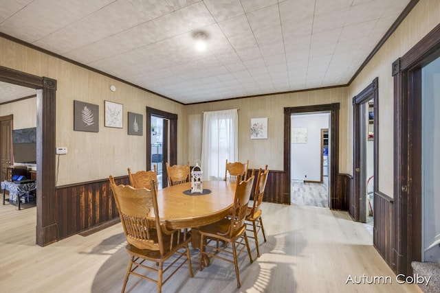 dining space with wooden walls, crown molding, and light wood-type flooring