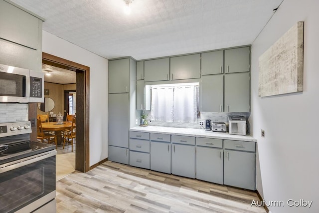 kitchen with backsplash, gray cabinetry, light countertops, light wood finished floors, and stainless steel appliances