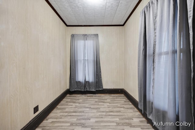 empty room with wooden walls, baseboards, ornamental molding, and wood finished floors