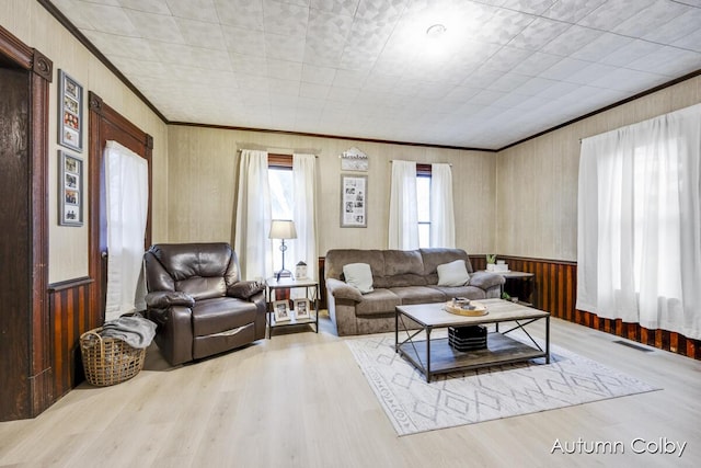 living room featuring crown molding, wood finished floors, wooden walls, and visible vents