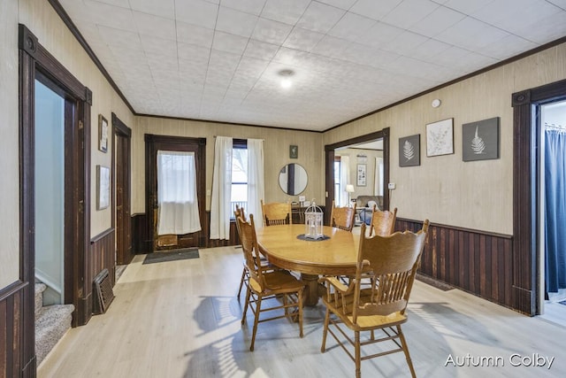 dining space featuring crown molding, wooden walls, stairs, and light wood finished floors