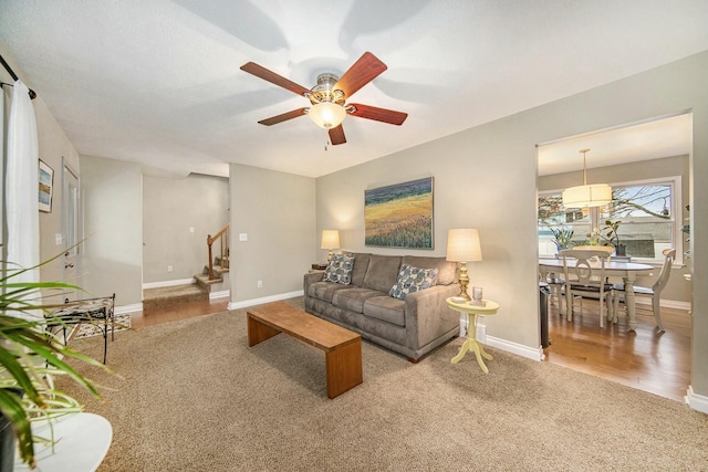 carpeted living area with stairs, baseboards, wood finished floors, and ceiling fan