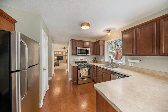 kitchen with light countertops, a textured ceiling, light wood-style floors, stainless steel appliances, and a sink