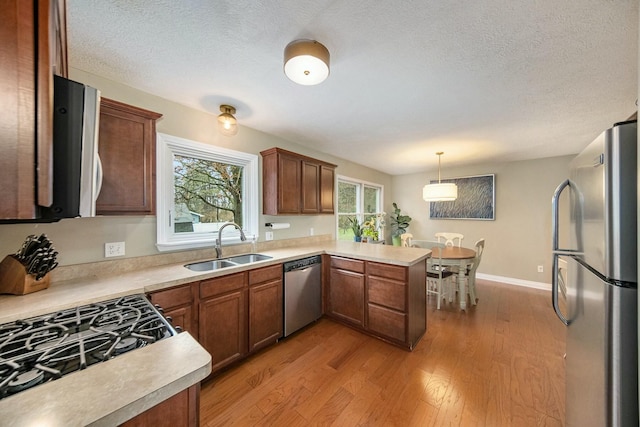 kitchen with a peninsula, light countertops, a sink, stainless steel appliances, and light wood finished floors